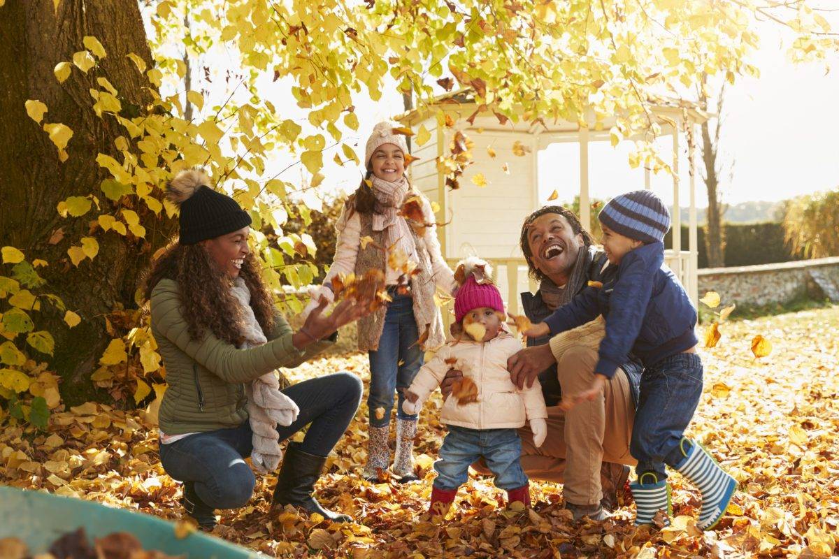 Children Helping Parents To Collect Autumn Leaves In Garden